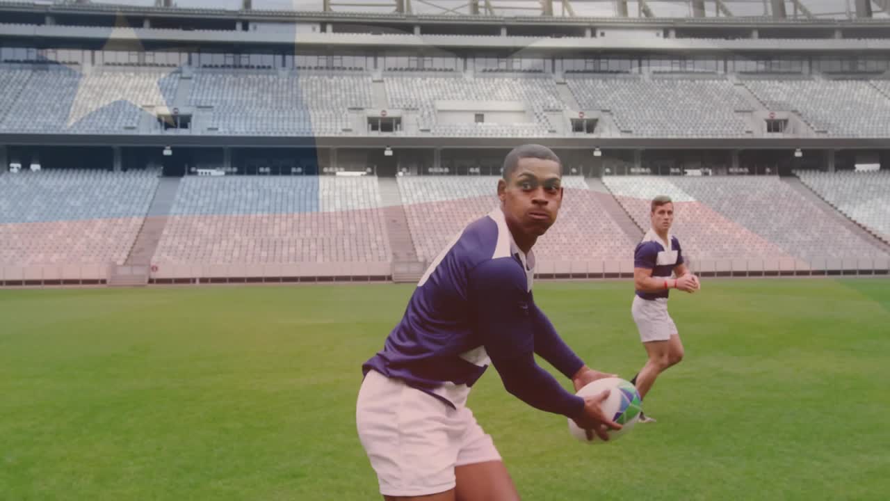 Trénink rugby, hráči běhají a přihrávají si míč na zeleném hřišti na stadionu.