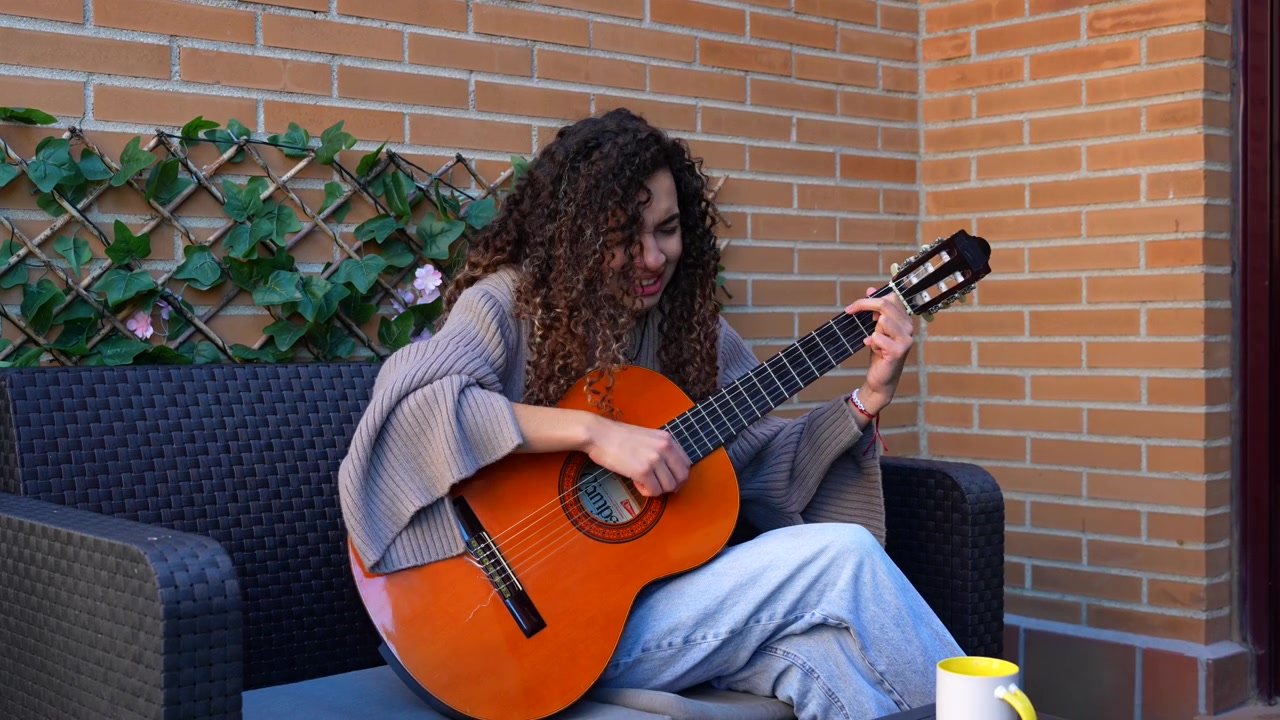 Talentfuld kvindelig musiker komponerer musik på en klassisk guitar, mens hun sidder på en terrassesofa