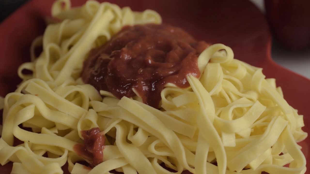 Pouring tomato sauce over freshly cooked tagliatelle pasta close up shot