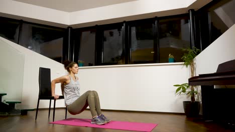 woman performing triceps dips on a chair in a home setting, evening indoor exercise routine