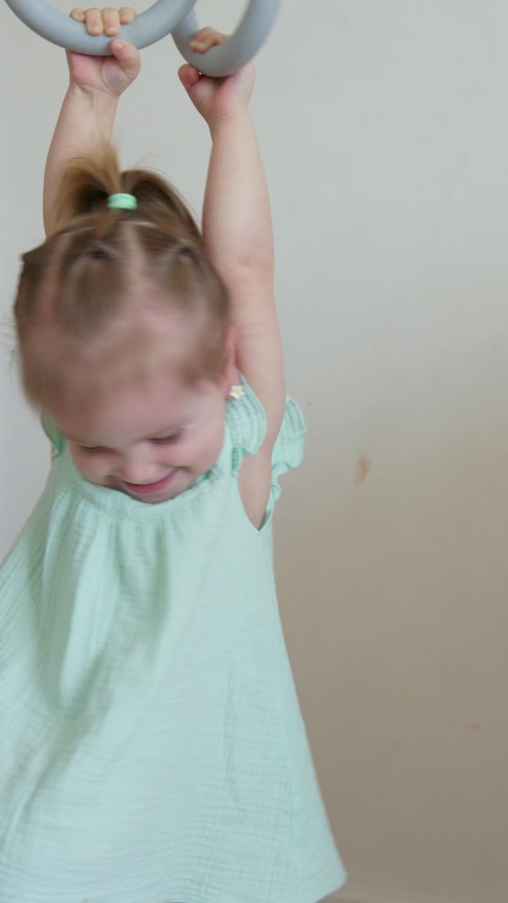 Happy Little Girl Playing and Hanging on Gymnastic Rings Indoors