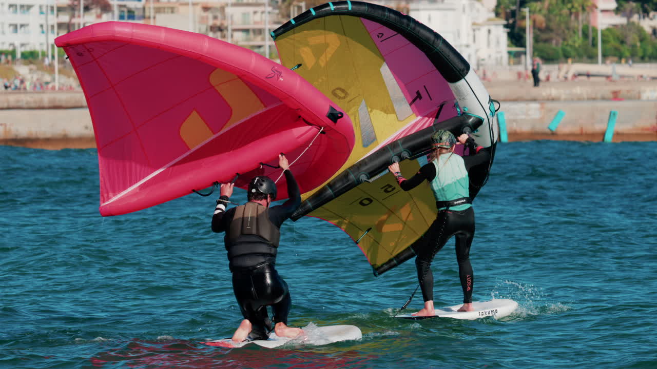 Cannes, France - October 6, 2025: A man and woman on wing foil boards holding colorful sails ride side by side on the turquoise sea