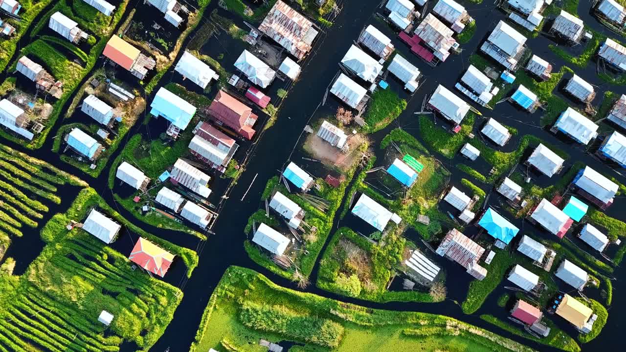 미마 인레 호수 (inle lake) 에 있는 집, 울창한 초록색 식물, 그리고 물 운하가 있는 떠다니는 마을의 공중 사진. 이 장면은 독특한 기둥집, 수로, 그리고 활기찬 농경지를 강조합니다.
