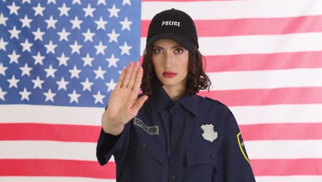 female police officer in uniform with american flag background making a stop gesture