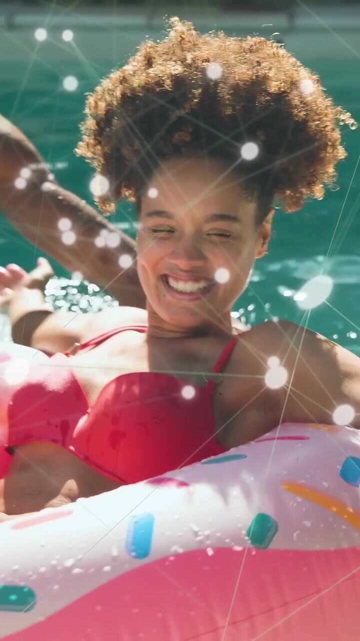 Vertical video: Woman on donut float playing, reaching as man tossing ball, ads overlay on float