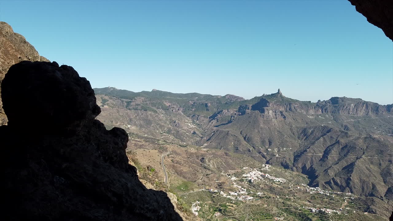 fantástica toma atravesando rocas y dejando ver el paisaje de la ciudad de tejeda y roque nublo a lo lejos