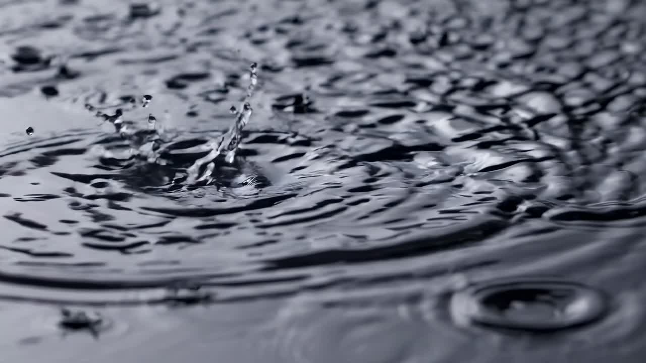 Nahaufnahme-Video von auf einer Wasseroberfläche spritzenden Regentropfen, aus einem niedrigen Winkel aufgenommen
