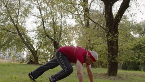 elderly sporty man doing push up exercises. workout cardio outside in city park at morning