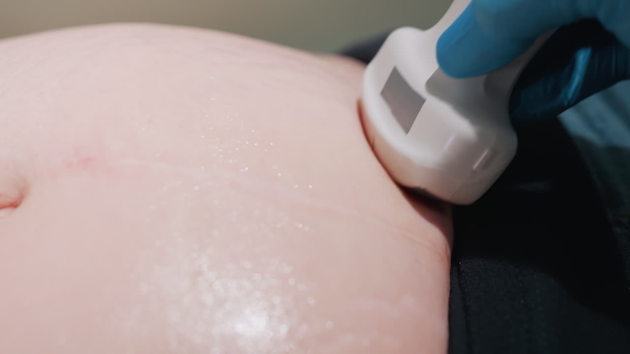 female lab technician in medical gloves rolling ultrasound scanner gently across abdomen of patient during clinical examination using scanning gel to improve contact for accurate internal imaging