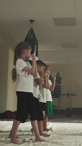 los niños se paran en postura de boxeo con el entrenador en el gimnasio. los estudiantes pequeños aprenden técnicas de autodefensa bajo el control del sensei en el club deportivo en cámara lenta