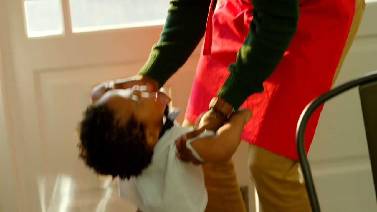 vista frontal de un joven padre negro jugando con su hijo en la cocina de una casa cómoda 4k