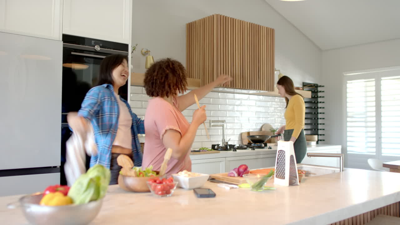 Cozinhando juntas na cozinha, três amigas diversas se divertindo ao preparar a refeição e dançando