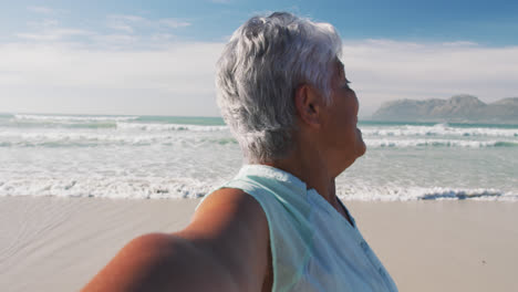 Mujer-Afroamericana-Mayor-Sonriendo-A-La-Cámara-Y-Caminando-En-La-Playa