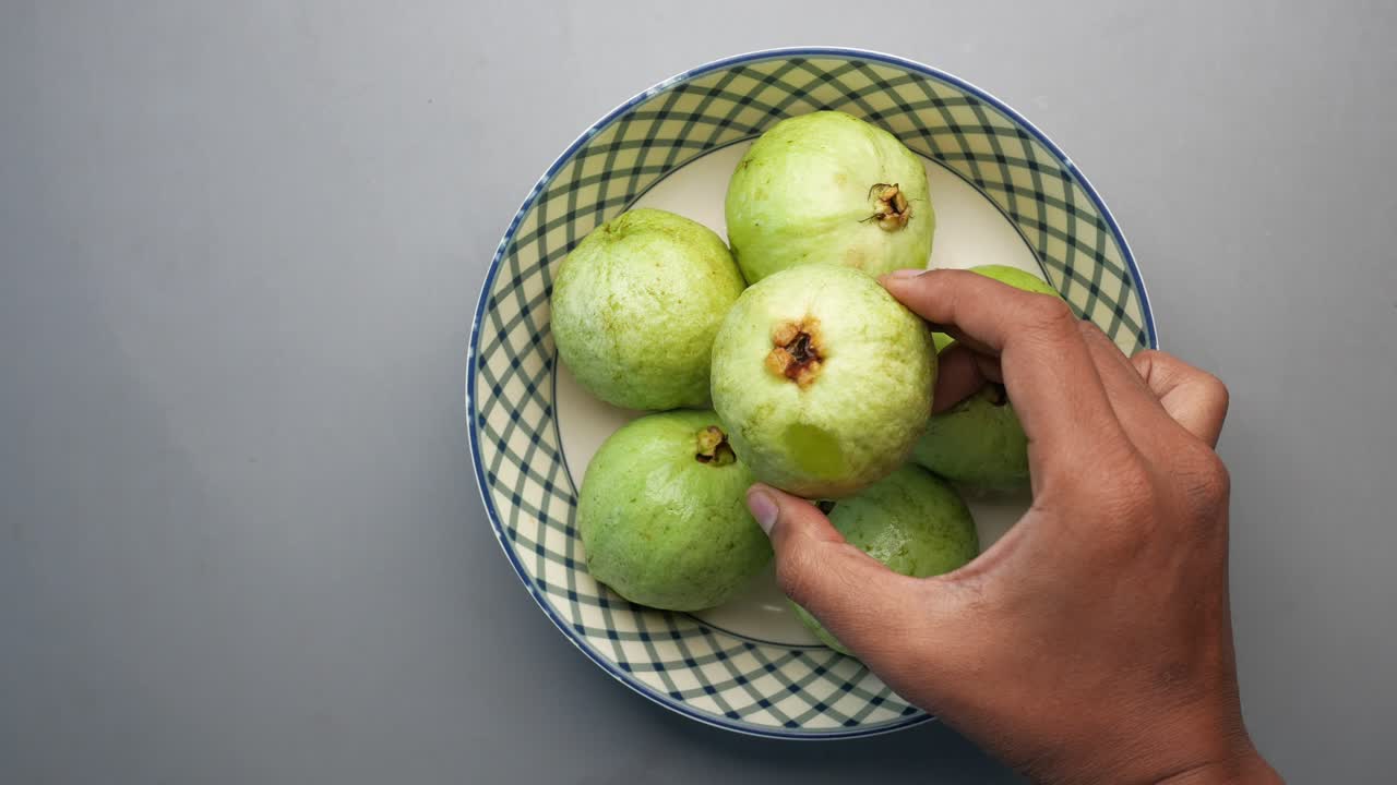 primer plano de una mano recogiendo una guayaba de un cuenco de guayabas frescas