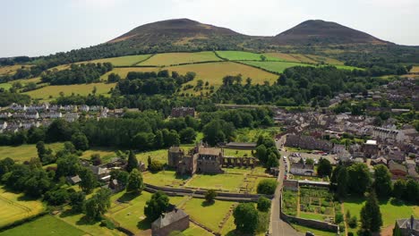 Aerial-shot-forward-of-beautiful-countryside-town-of-Melrose-and-bright-green-and-yellow-fields-during-spring-in-the-Scottish-Borders-showing-rural-landscapes-near-Edinburgh,-Scotland,-United-Kingdom