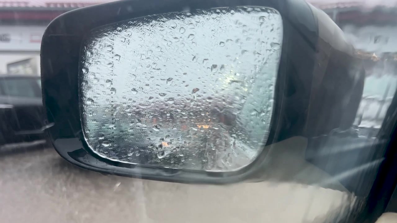 Primo piano di goccioline d'acqua su uno specchietto retrovisore di un veicolo durante una giornata piovosa. Autentica atmosfera cinematografica per concetti di viaggio, meteo e sicurezza