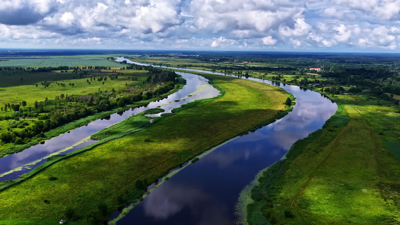 Drone view of rivers winding through lush, green landscape and cumulus clouds in sky
