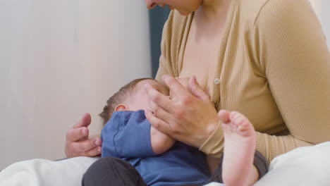 close up of a young mother breastfeeding her baby boy while sitting on the bed at home