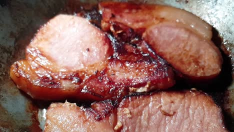 slow motion pan of pork chops meat in cast iron frying pan with olive oil for food presentations, almost done and ready to be served