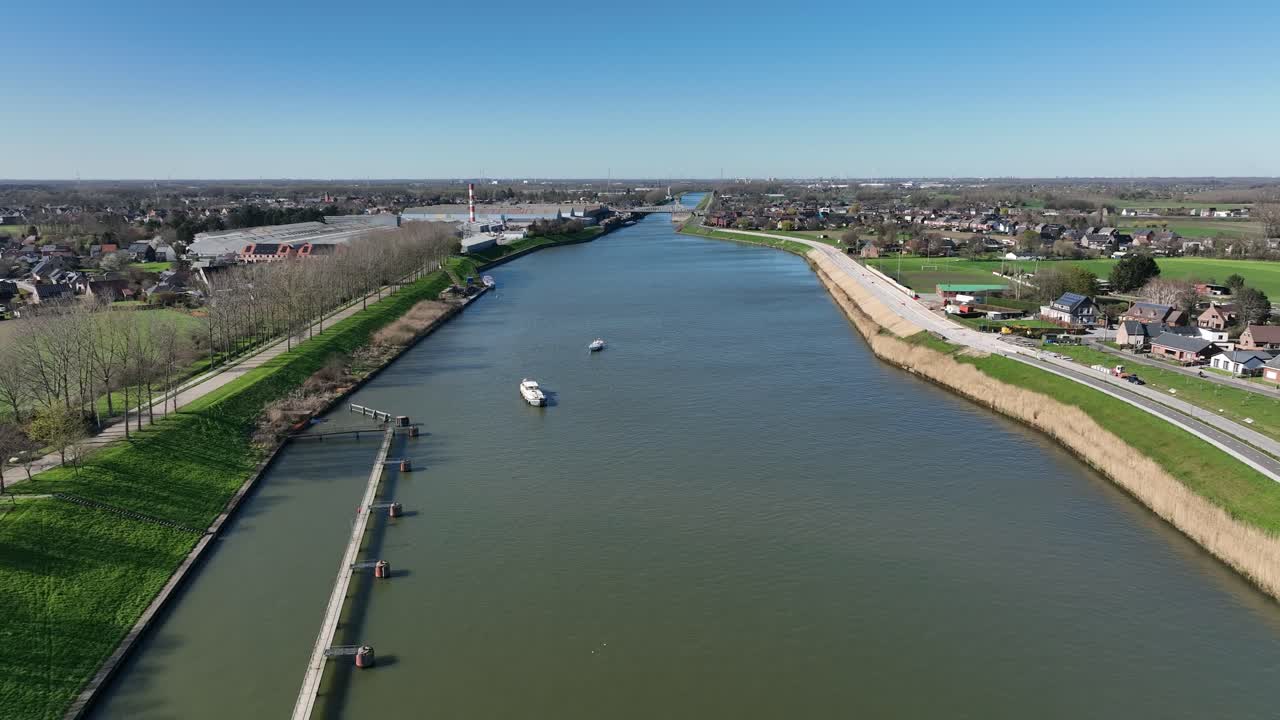 Aerial zoom out showing Antwerp canal with boats navigating through rural landscape, surrounded by trees, fields, and small villages