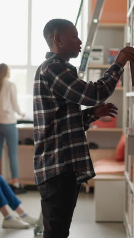 man takes book from shelf in city public library. african american customer seeks textbook working with students in information center. bookstore visitors