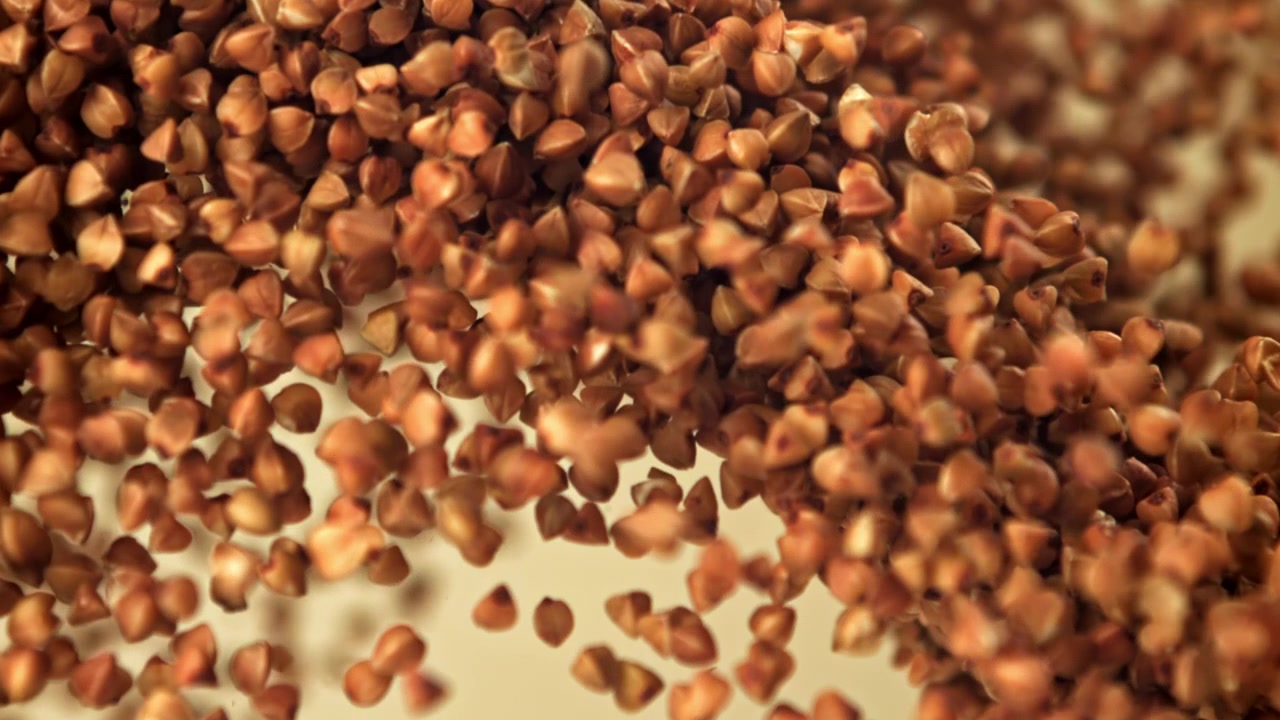 Chicchi di grano saraceno crudo che cadono e si accumulano al rallentatore.