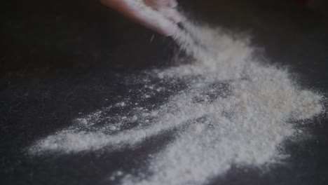 mano de mujer arrojando harina de pizza sobre una mesa de mármol en la cocina