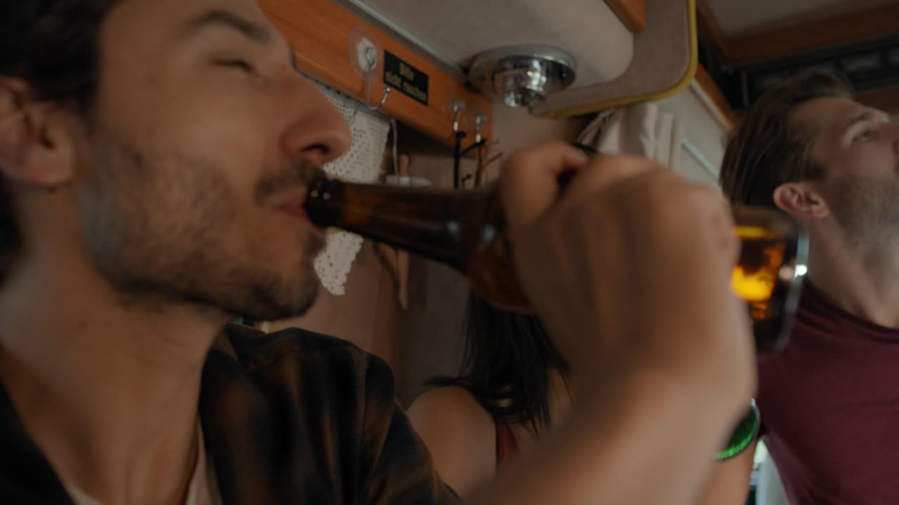 Young friends spending time inside the camper on drinking beer and relaxing.