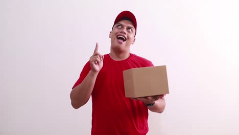 Young-asian-courier-man-holding-packet-on-cardboard-while-pointing-above