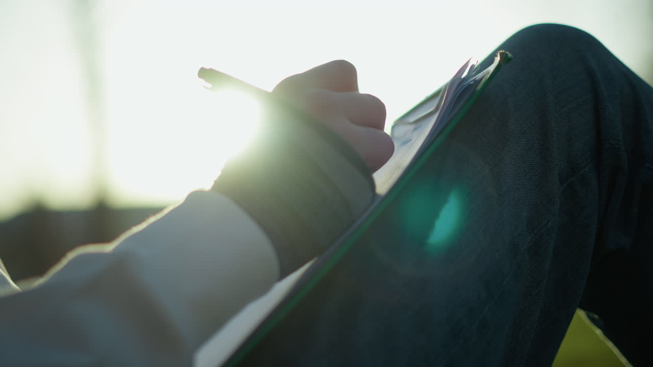 創造的に屋外でスケッチする女性アーティスト、夕焼け時に屋外で自然の風景を描く穏やかな女性、夕暮れ時に草の生えた丘の斜面で風景を捉えるリラックスした女性イラストレーター