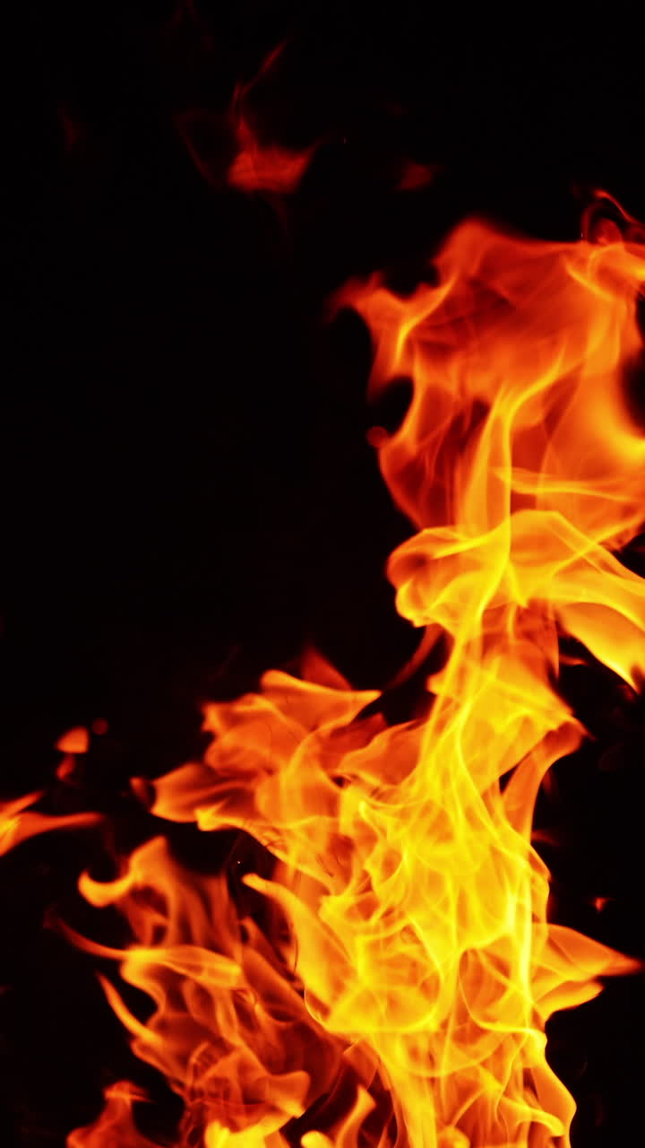 Fiamme, fumo e piccole scintille che volano via. Falò ardente in una notte buia. Primo piano. Video verticale