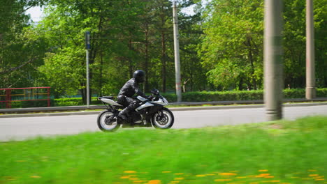 Un-Ciclista-Recorre-Una-Motocicleta-A-Lo-Largo-De-Una-Gran-Carretera-Que-Pasa-Por-Un-Parque-Verde