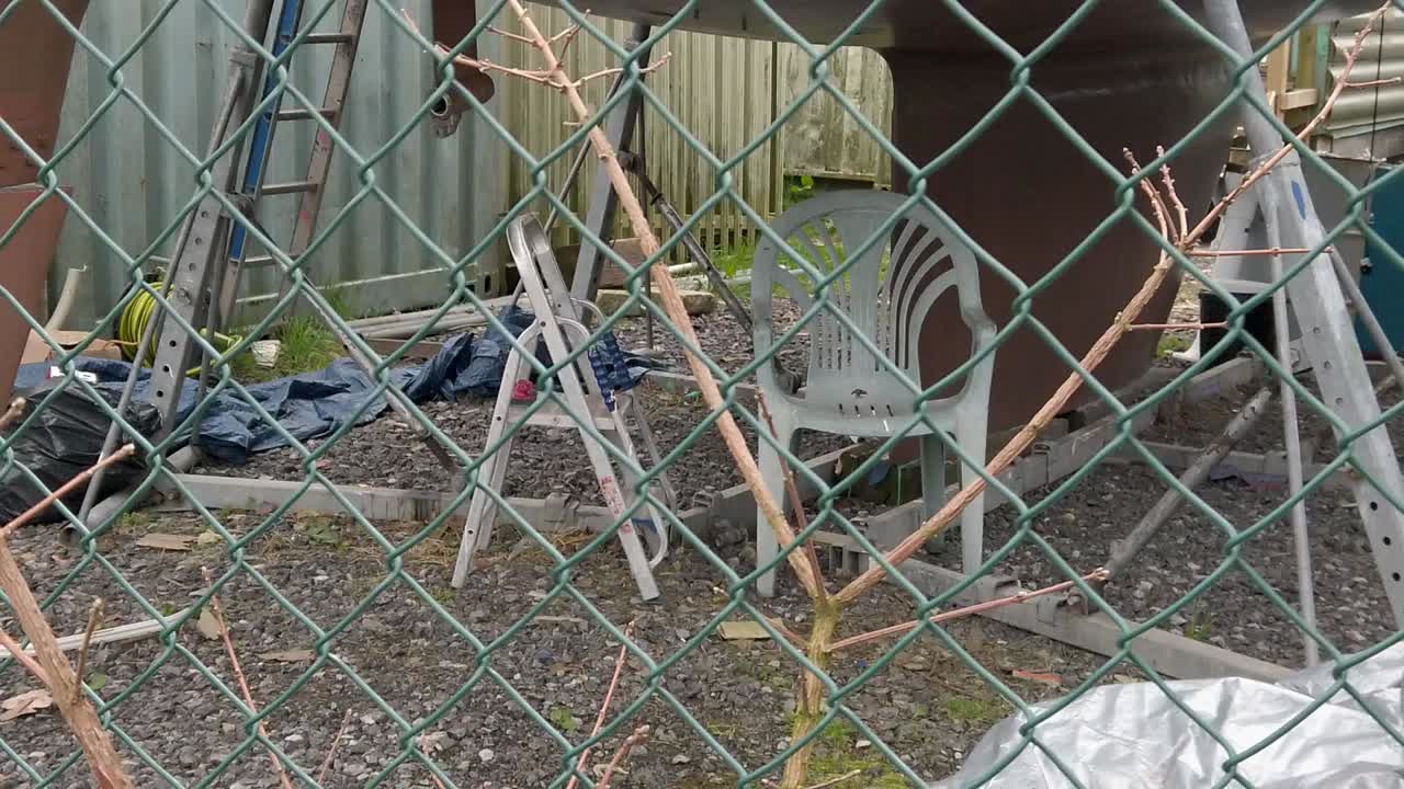 silla de jardín de plástico y escalera bajo el proyecto de renovación del casco del barco en el astillero dolly más allá de la valla segura