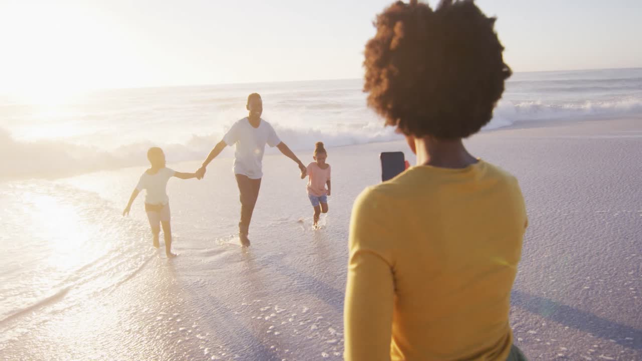 Smiling african american family taking photo and walking on sunny beach