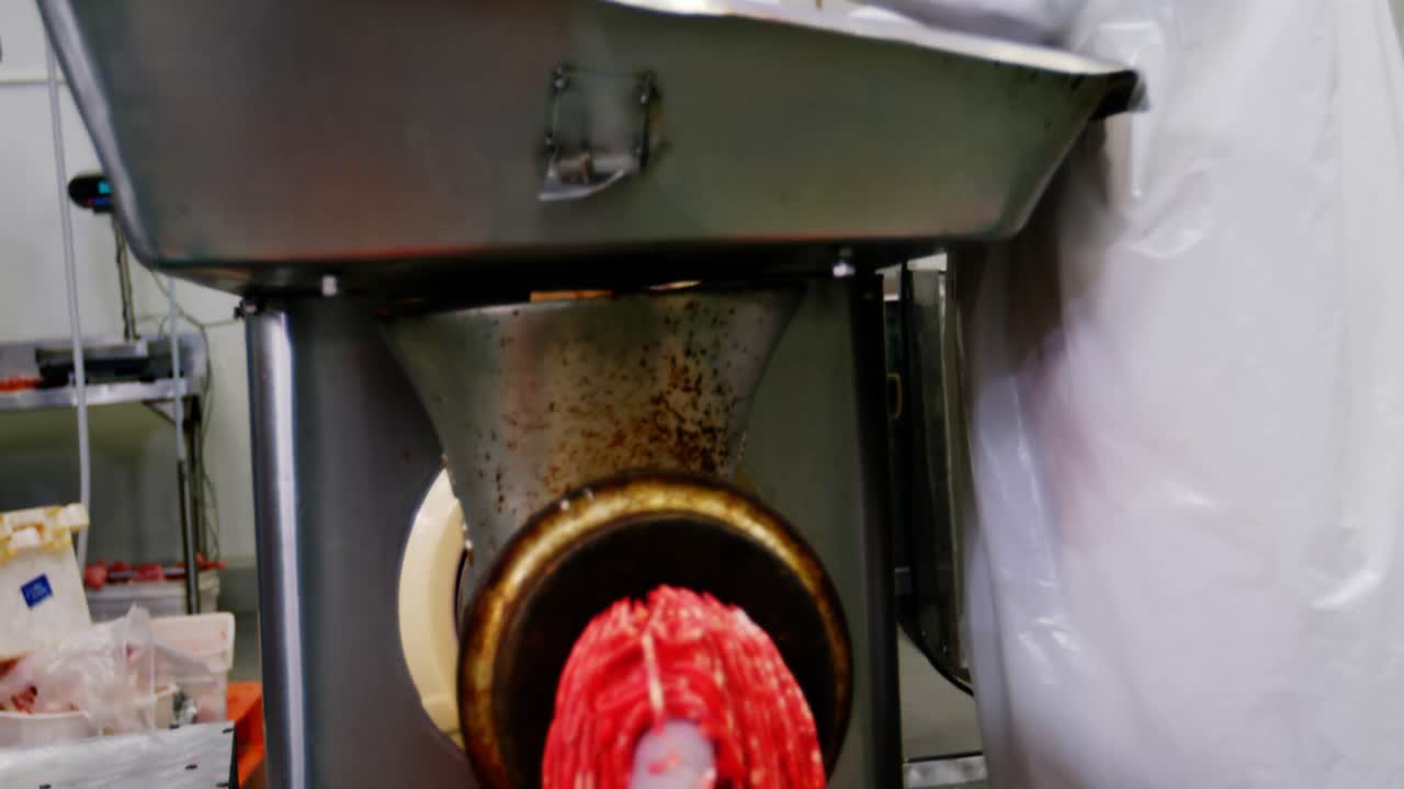 Tukang daging memasukkan daging ke dalam mesin penggiling