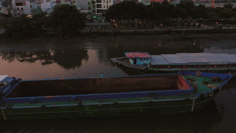 Tiro-Nocturno-De-Drones-De-Dos-Grandes-Cargueros-Fluviales-Están-Pasando-Cada-Uno-En-Un-Canal-Estrecho-En-La-Ciudad-De-Ho-Chi-Minh,-Vietnam