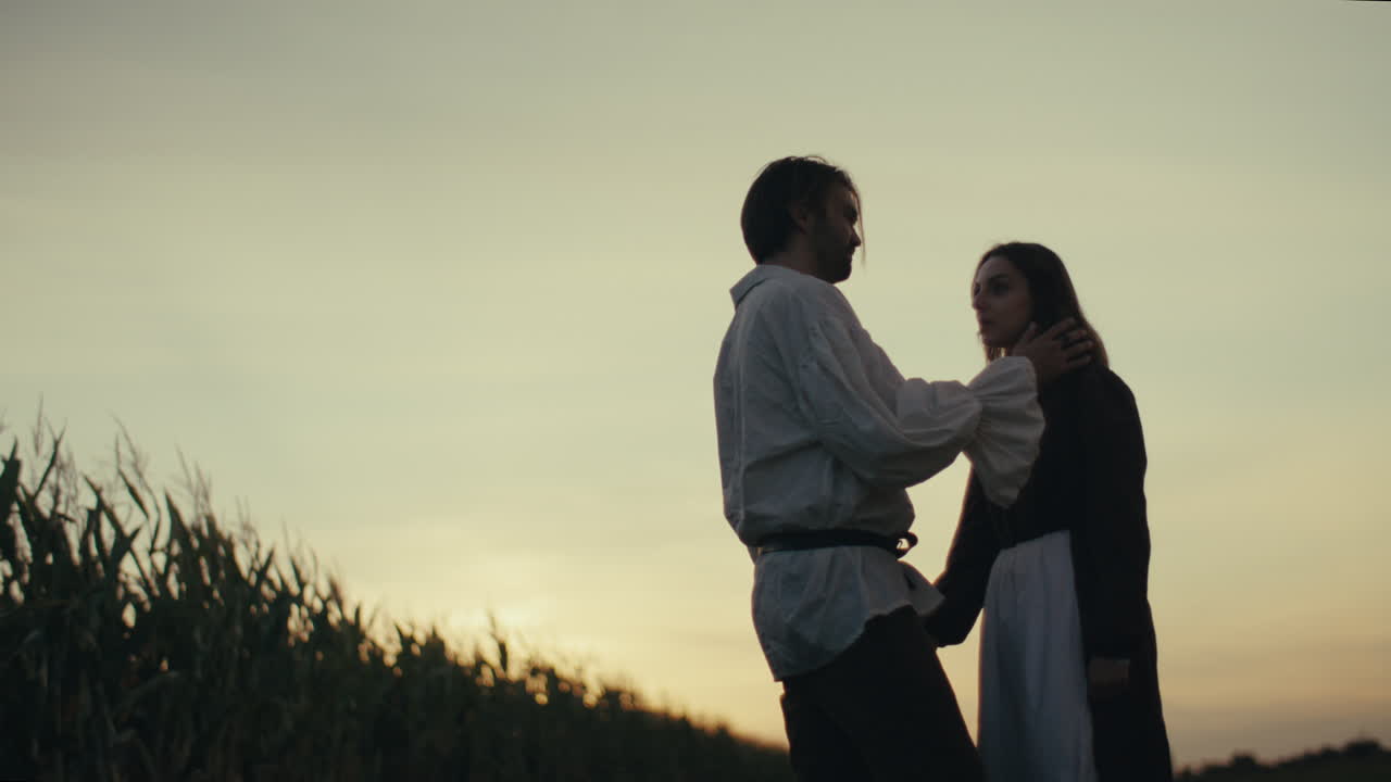 A couple in period attire embracing in a field at sunset
