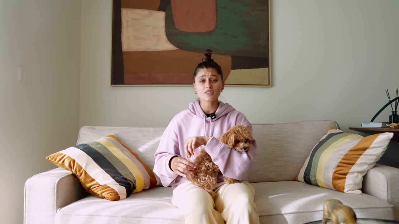 Ung kvinne sitter i sofaen med sin lille hund og snakker