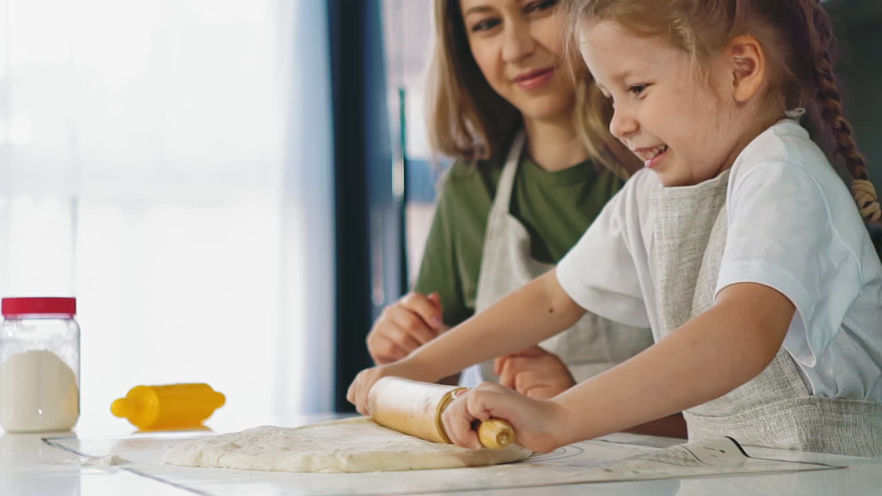 girl in apron rolls dough cooking with mother at table