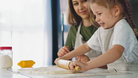 girl in apron rolls dough cooking with mother at table