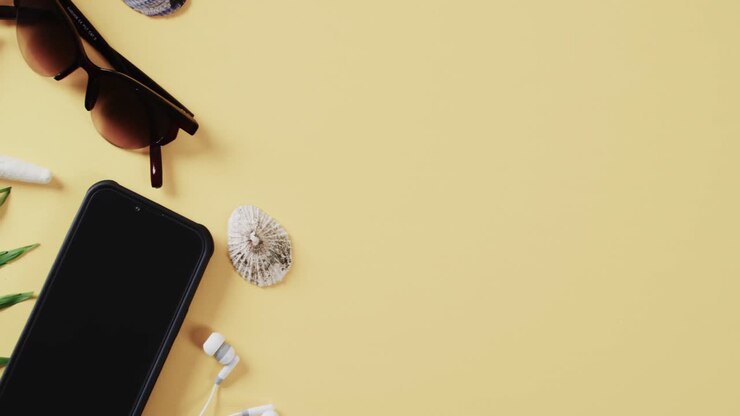 Close up of shell, smartphone and sunglasses with copy space on yellow background