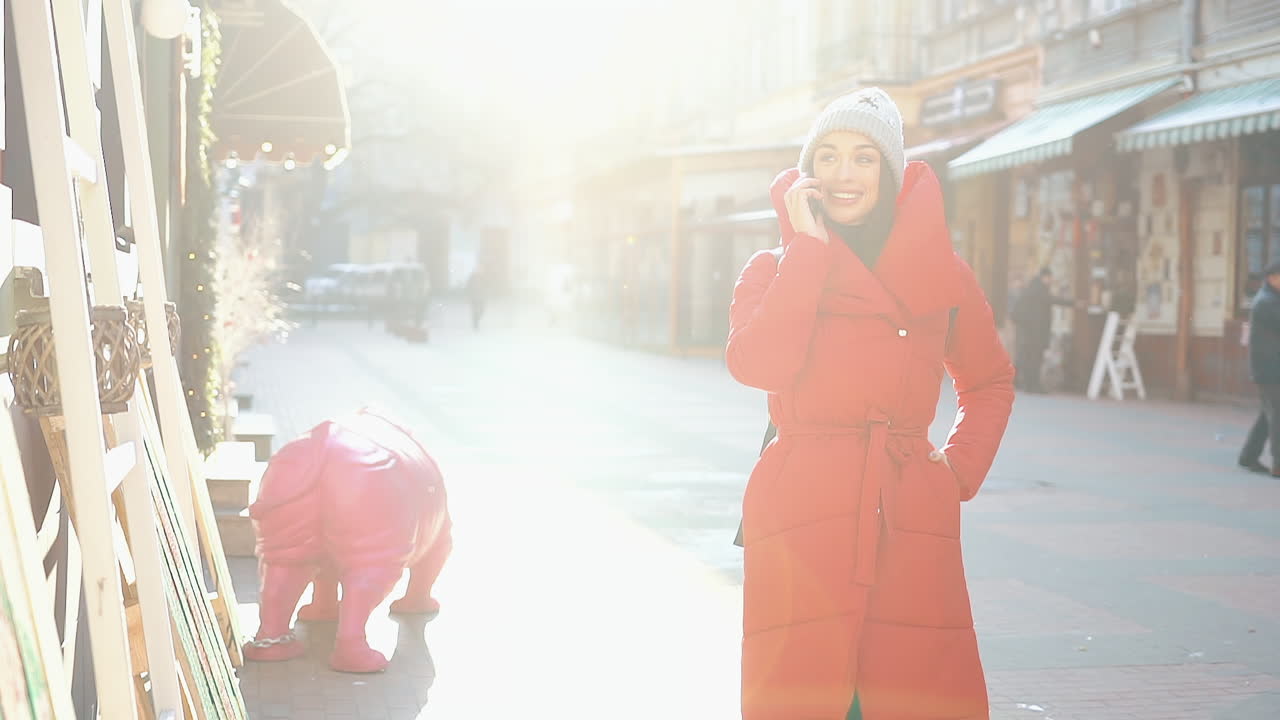 Woman in red puffer coat talking on the phone in a city street
