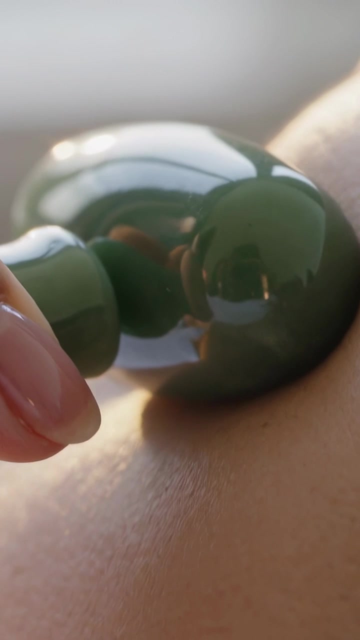 Vertikal video: Hånd kommer ind og skubber til en olivengrøn perle på armen i et rum, der viser hud og telefon.