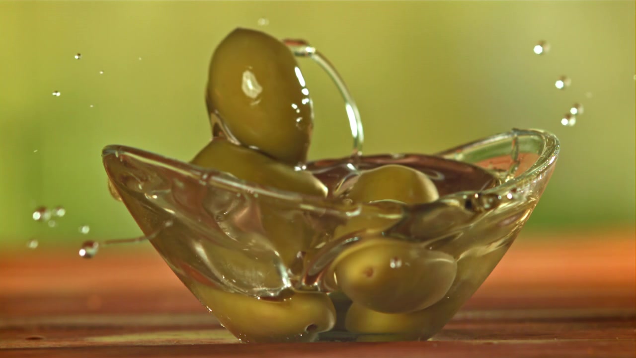 Olive verdi fresche che cadono nell'olio d'oliva in una ciotola di vetro