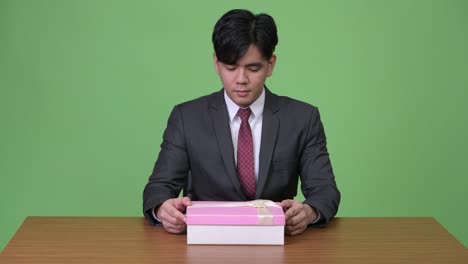 young asian businessman looking happy and surprised while opening gift box