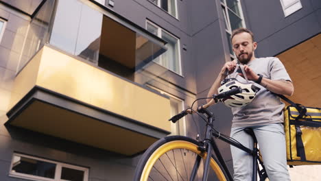 food delivery man wearing thermal backpack recorded from below puts on a helmet and start riding his bike