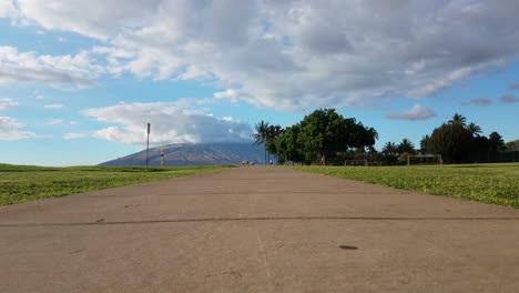 Vista-De-ángulo-De-Cámara-Inferior-De-Una-Acera-Con-Gente-Caminando-En-La-Distancia-Con-Lanai-Y-Las-Montañas-Del-Oeste-De-Maui-En-El-Fondo-Justo-Antes-Del-Atardecer-En-Kihei-Maui-Hawaii