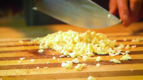 garlic is being minced with a chef's knife on a striped wooden cutting board