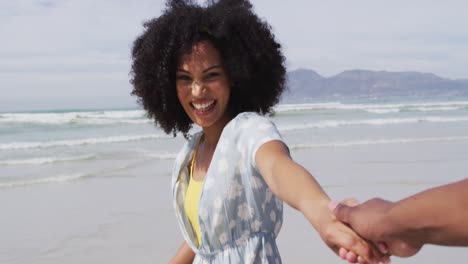 una pareja afroamericana sonriente caminando y tomados de la mano en la playa