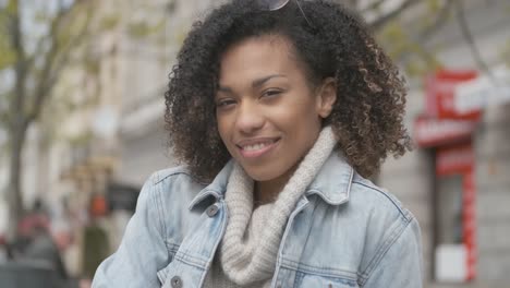 adorable chica con corte de pelo afro sentada en un banco en la calle de la ciudad